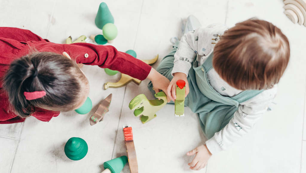 Two children playing with wooden dinosaur toys